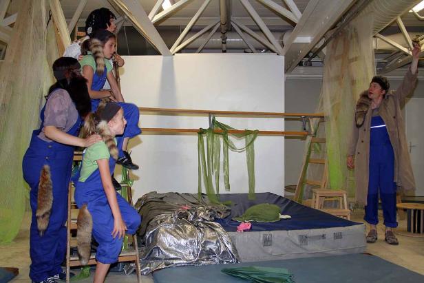 Eine Theaterszene mit Kindern und einem Erwachsenen in Kostümen mit Waschbärschwänzen.