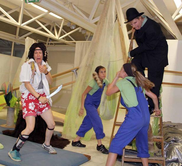 Eine Theaterszene mit einer verängstigten Person mit Machete und drei weiteren Darstellern.