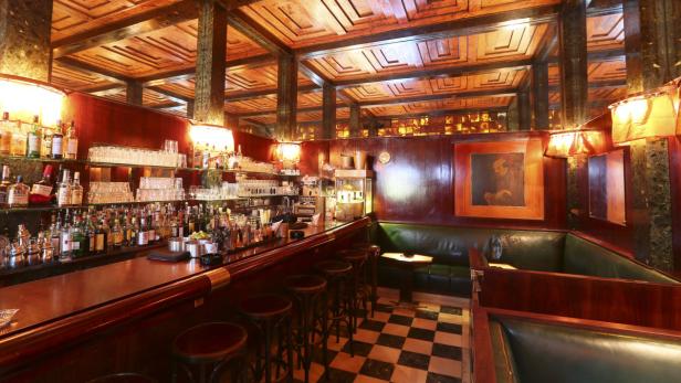 Eine Bar mit dunkler Holzvertäfelung, Schachbrettboden und grünen Ledersitzbänken.