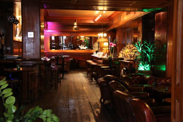 Innenansicht einer Bar mit dunkler Holzvertäfelung und Ledersesseln.