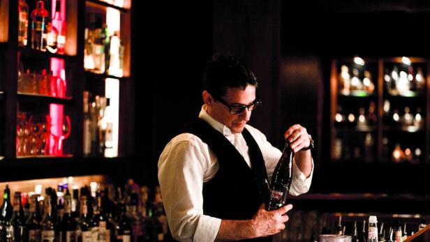Ein Barkeeper mit Brille betrachtet eine Flasche Havana Club vor einer Bar.