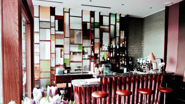 Eine Bar mit Hockern und einer Wand aus dekorativen Glaselementen.