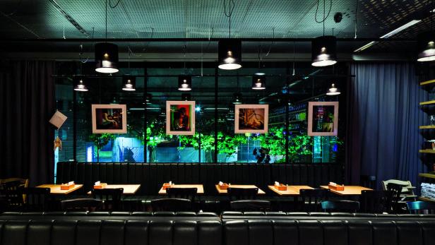 Innenansicht eines Restaurants mit Tischen, Stühlen und gerahmten Bildern an der Wand.