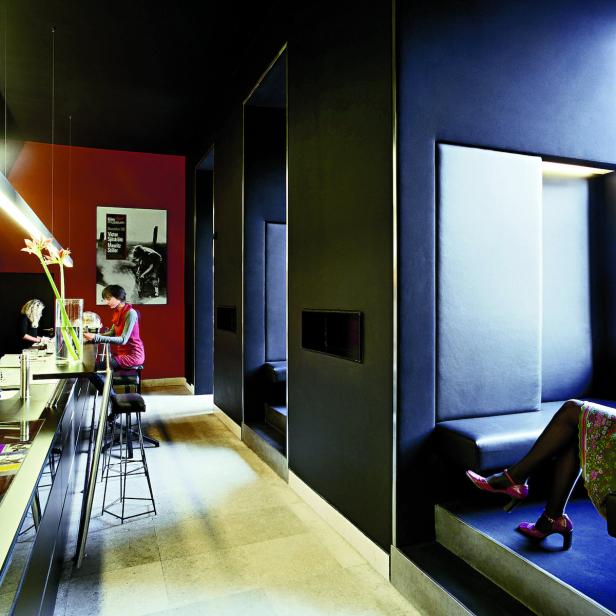 In einem eleganten Café sitzt eine Frau an der Bar, während eine andere in einer Sitzecke entspannt.