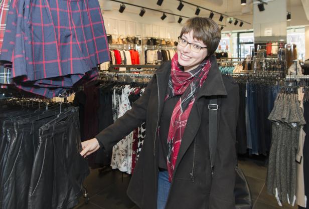 Eine Frau mit Brille und Schal steht in einem Bekleidungsgeschäft.