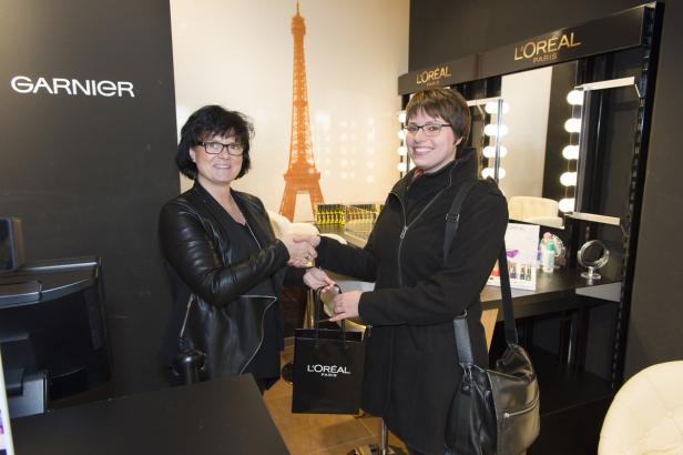 Zwei Frauen schütteln sich die Hände vor einem L'Oréal-Stand mit einem Eiffelturm-Motiv.