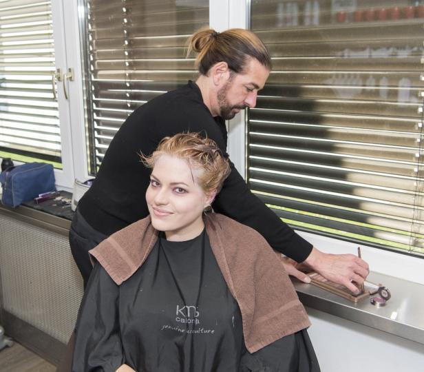 Eine Frau sitzt beim Friseur, während ein Friseur ihre Haare macht.