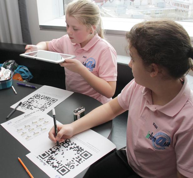 Zwei Mädchen arbeiten an einem Tisch mit QR-Codes und einem Tablet.