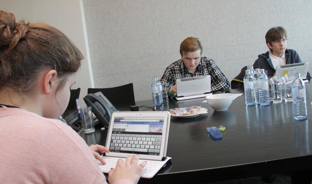 Mehrere Personen sitzen an einem Tisch und arbeiten an Tablets.