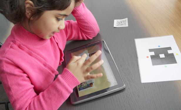 Ein junges Mädchen mit einem pinkfarbenen Pullover benutzt ein Tablet.