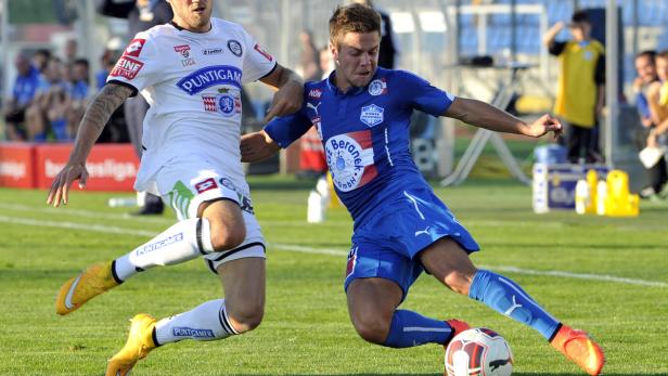 Zwei Fußballspieler kämpfen um den Ball auf dem Rasen.