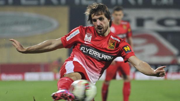 Ein Fußballspieler in roter Spielkleidung schießt einen Ball.