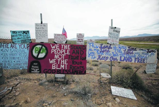 Mehrere Schilder mit politischen Botschaften stehen an einem Zaun in einer trockenen Landschaft.