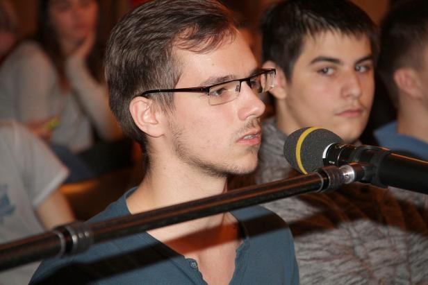 Ein junger Mann mit Brille spricht in ein Mikrofon.