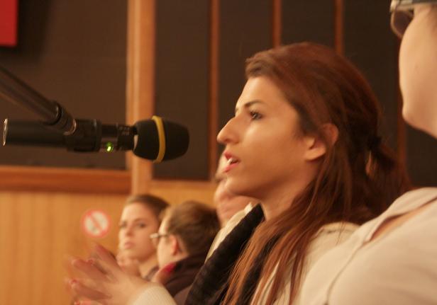 Eine Frau spricht in ein Mikrofon vor einem Publikum.