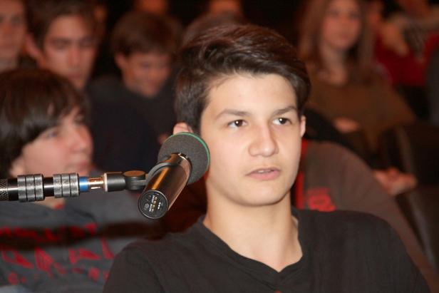 Ein junger Mann spricht in ein Mikrofon vor einem Publikum.