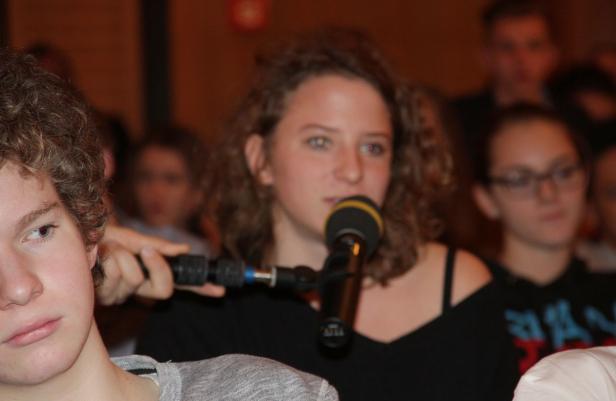 Eine junge Frau spricht in ein Mikrofon vor einem Publikum.