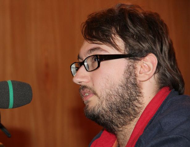 Ein Mann mit Bart und Brille spricht in ein Mikrofon.