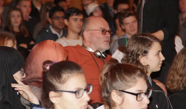 Ein Publikum sitzt bei einer Veranstaltung, darunter ein Mann mit Kopfhörern.