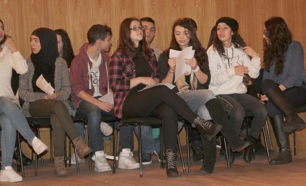 Eine Gruppe junger Leute sitzt auf Stühlen und hält Papiere in der Hand.