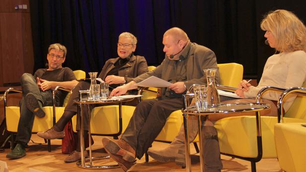 Vier Personen sitzen auf gelben Sesseln auf einer Bühne und diskutieren.