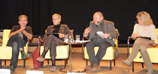 Vier Personen sitzen auf gelben Stühlen auf einer Bühne und nehmen an einer Podiumsdiskussion teil.