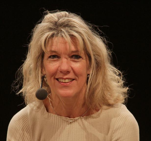 Eine blonde Frau mit Mikrofon lächelt in die Kamera.