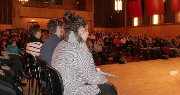Zuschauer sitzen in einem Hörsaal und verfolgen eine Präsentation.