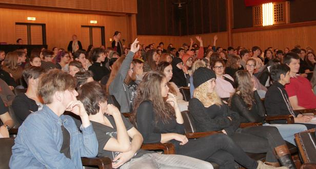Ein Publikum sitzt in einem Auditorium, einige Personen heben die Hände.