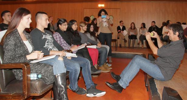 Eine Gruppe von Menschen sitzt in einem Raum, während ein Mann sie mit seinem Handy fotografiert.