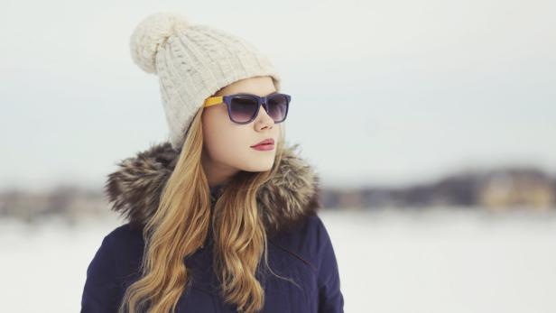 Eine Frau mit Sonnenbrille und Wintermütze blickt in die Ferne.