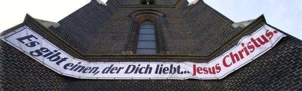 Eine Kirche mit einem Banner, auf dem steht: „Es gibt einen, der Dich liebt… Jesus Christus.“.