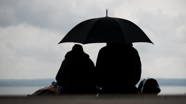 Zwei Personen sitzen im Schatten eines Regenschirms am Ufer.