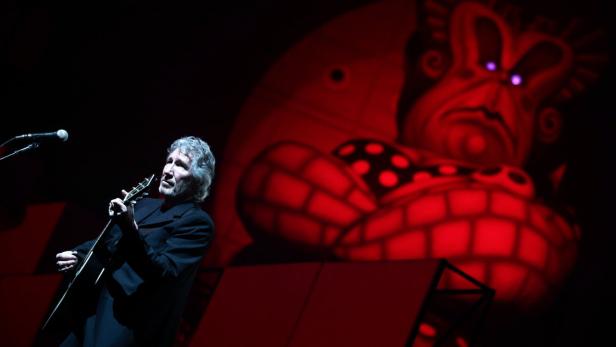 Roger Waters spielt Gitarre vor einer roten Projektion während eines Konzerts.