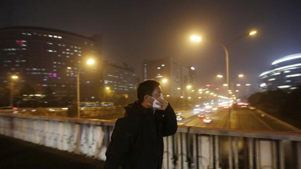 Ein Mann mit Maske steht nachts auf einer Brücke in einer Stadt.