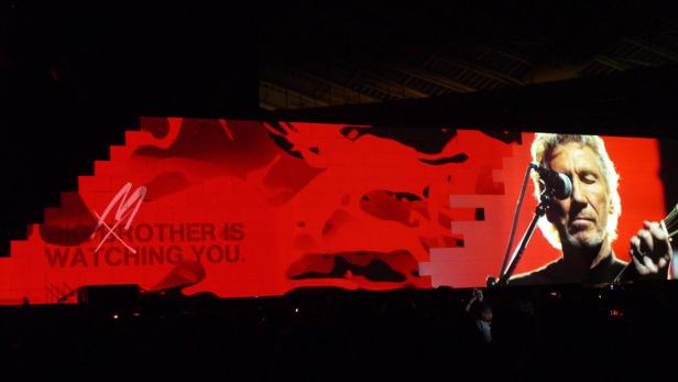 Roger Waters tritt auf einer Bühne mit der Aufschrift „Big Brother is watching you“ auf.