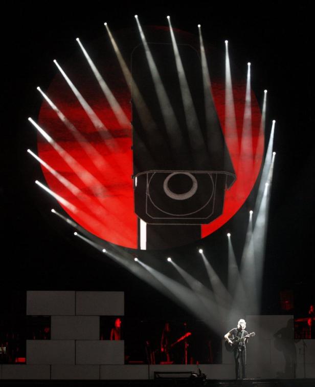 Roger Waters tritt mit Gitarre vor einer Projektion von „The Wall“ auf.