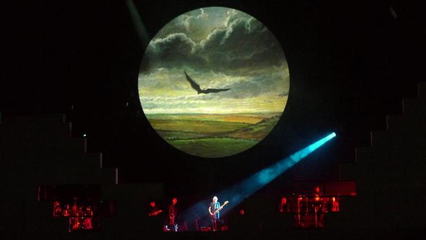 Eine Band spielt auf einer Bühne vor einer Projektion mit einem Adler über einer Landschaft.