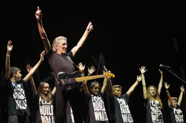 Roger Waters mit einer Bassgitarre und einer Gruppe von Kindern auf der Bühne.