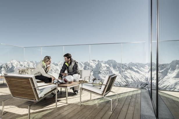 Ein Paar sitzt auf einer Terrasse mit Blick auf schneebedeckte Berge.
