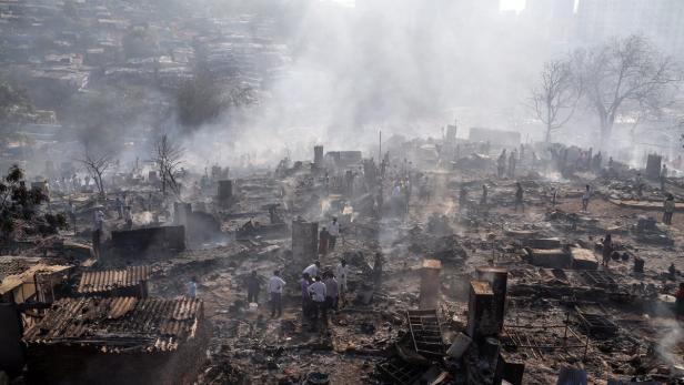 Nach einem Brand stehen Menschen inmitten der zerstörten Hütten eines Slums.
