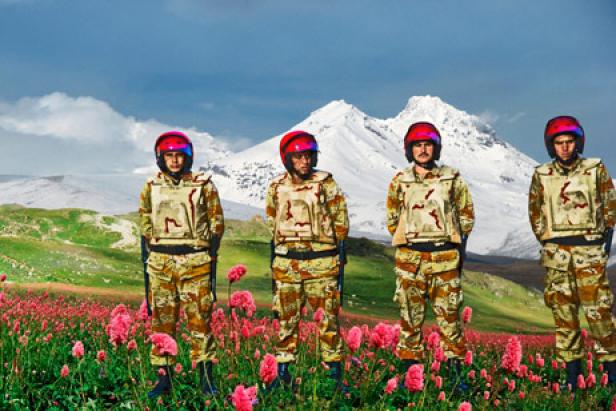 Vier Personen in Tarnkleidung und Helmen stehen auf einer Blumenwiese vor einem Berg.