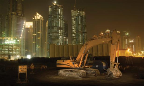 Ein Bagger steht nachts vor einer Skyline mit Hochhäusern.