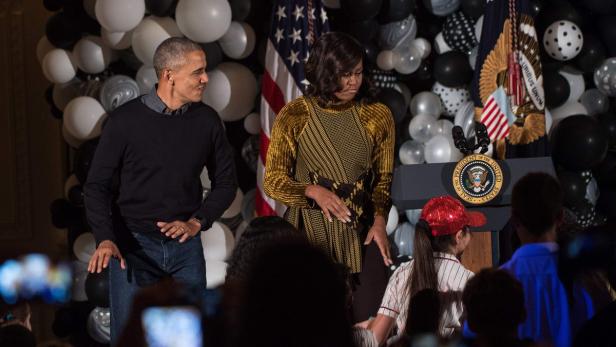 Barack und Michelle Obama stehen vor einer Menschenmenge und einer Dekoration aus Ballons.