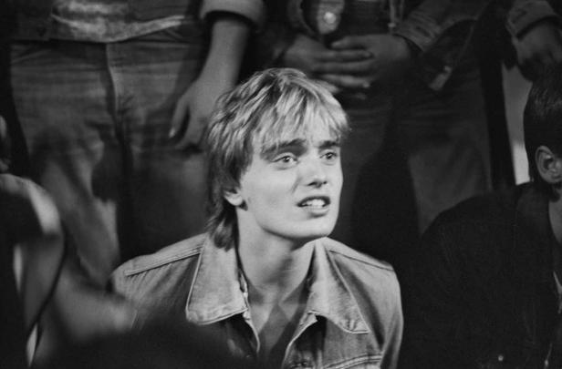 Ein junger Mann mit blonden Haaren und Jeansjacke schaut aufmerksam nach oben.