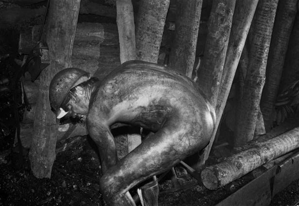 Ein Bergmann arbeitet in einem dunklen Stollen, gestützt durch Holzstämme.