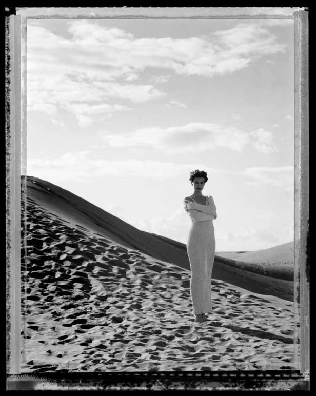 Eine Frau in einem langen Kleid steht in einer Sanddüne.
