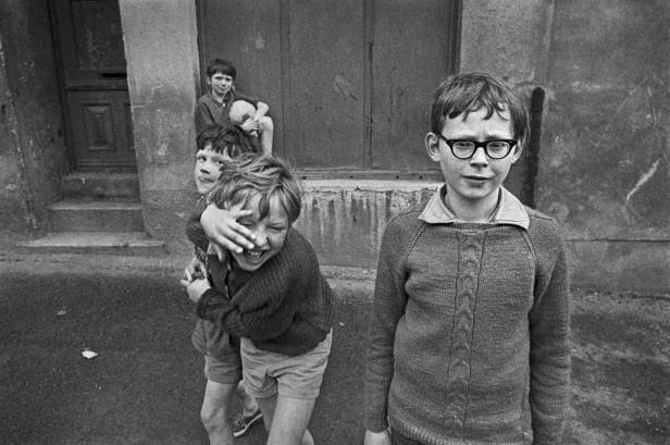 Eine Gruppe Jungen spielt in einer Gasse, einer davon trägt eine Brille.