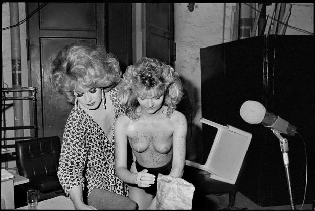 Zwei Performerinnen backstage, eine mit aufwendigem Make-up und die andere mit Glitzer auf dem Oberkörper.