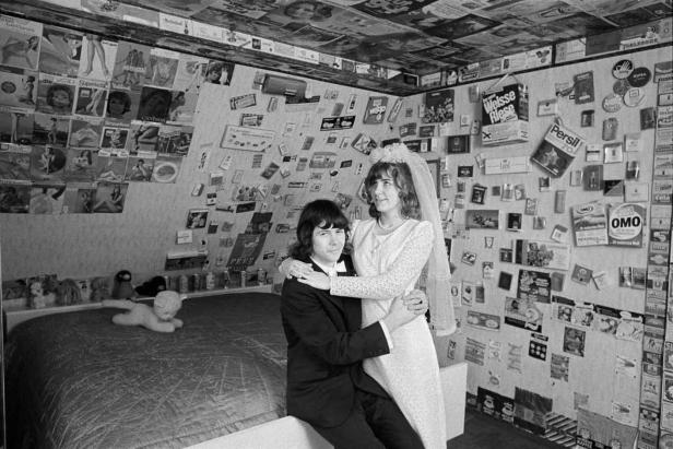 Ein frisch vermähltes Paar steht in einem mit Werbung beklebten Raum.